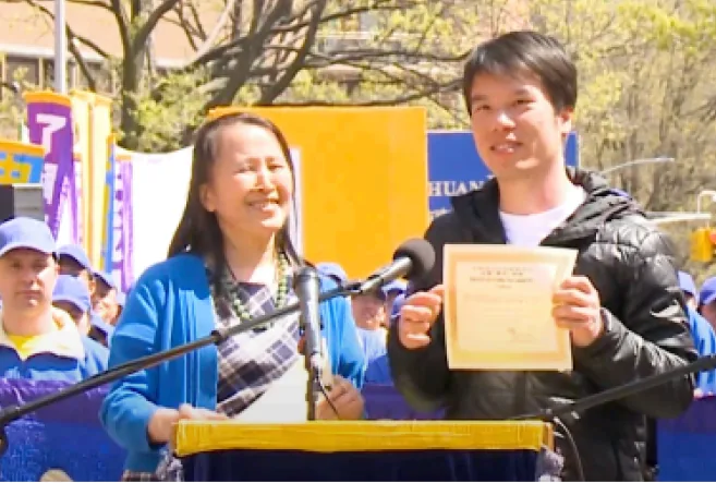 Um jovem segura um certificado de Tuidang em uma manifestação nos Estados Unidos, ao lado de Yi Rong, a presidente do Centro Global para Renunciar ao Partido